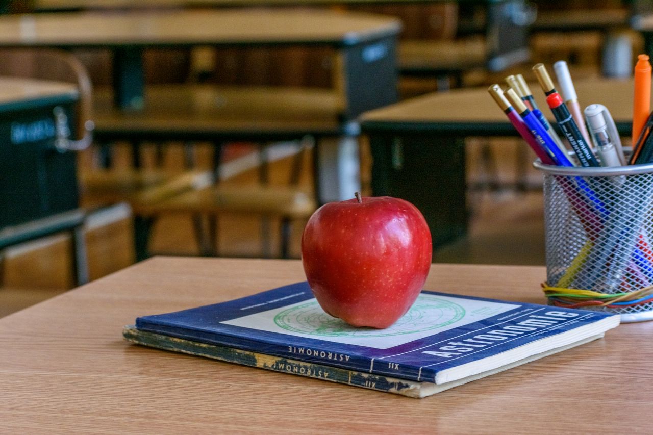 Red apple on books with stationery in a classroom, symbolizing education and knowledge.