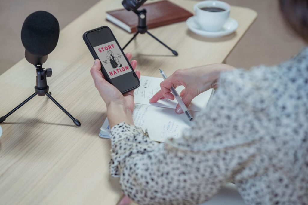 Demo Post 2 Back view faceless female in stylish blouse browsing mobile phone while sitting at desk with microphones and diary during interview
