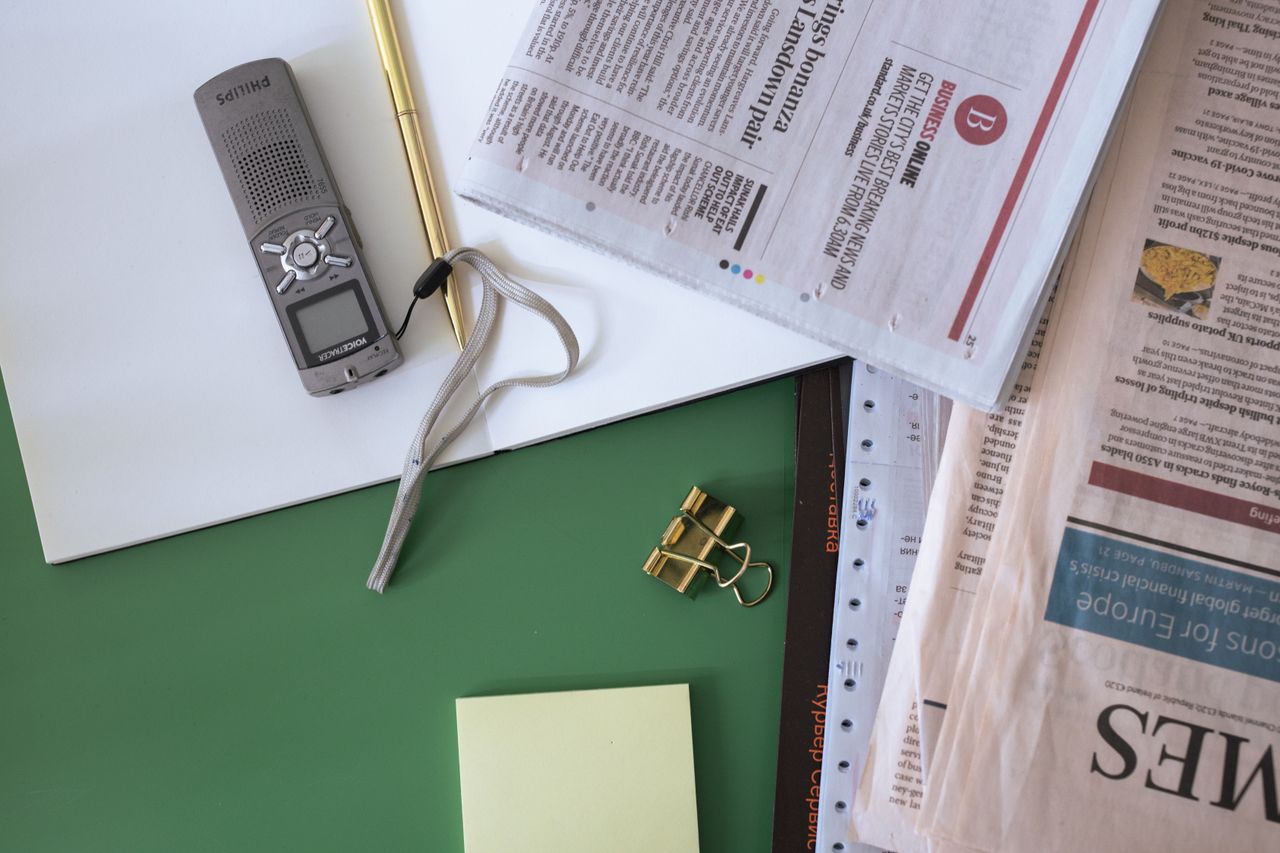 About Flat lay of an office desk with newspapers, notepad, and recorder on a green surface.